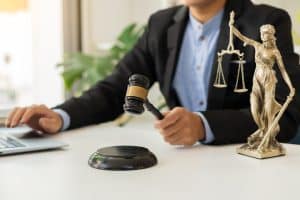 the goddess of justice with scales and hammers placed in front of a Male lawyer working on a laptop legal concept. Advice on Justice in the Lawyer's Office