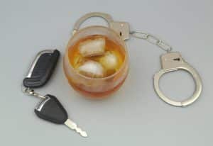 Glass with alcohol, steel handcuffs and car key on gray background.