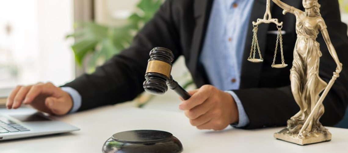 the goddess of justice with scales and hammers placed in front of a Male lawyer working on a laptop legal concept. Advice on Justice in the Lawyer's Office